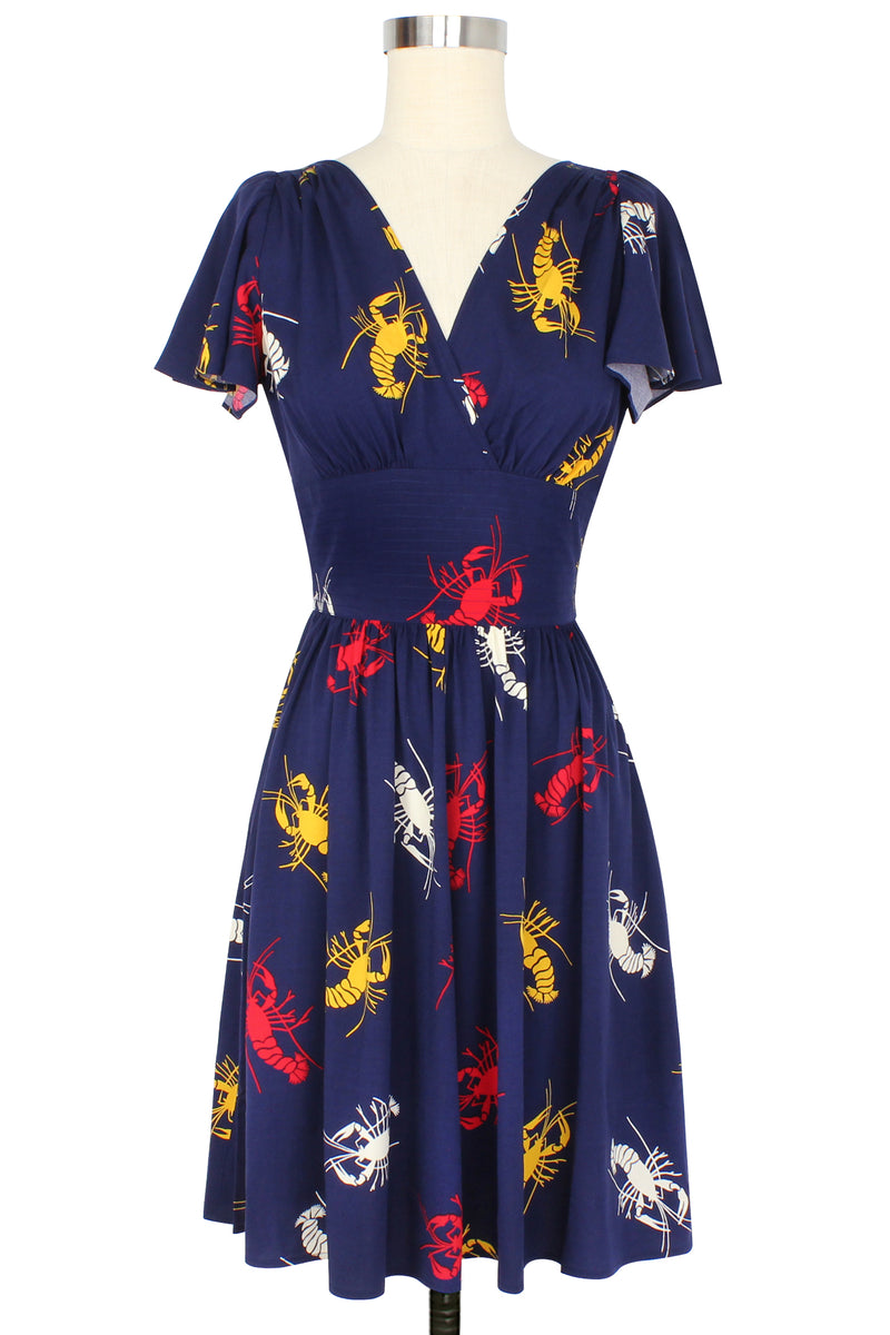 Take New Orleans home with you with our vintage-inspired Camilla Dress! This retro dress features flirty flutter sleeves before a fitted waistband, above-or-knee-length gathered skirt with pockets in our 1930s 1940s Crawfish novelty print of red, yellow, and white crustaceans on a deep navy blue background as a nod to Schiaparelli's lobster.