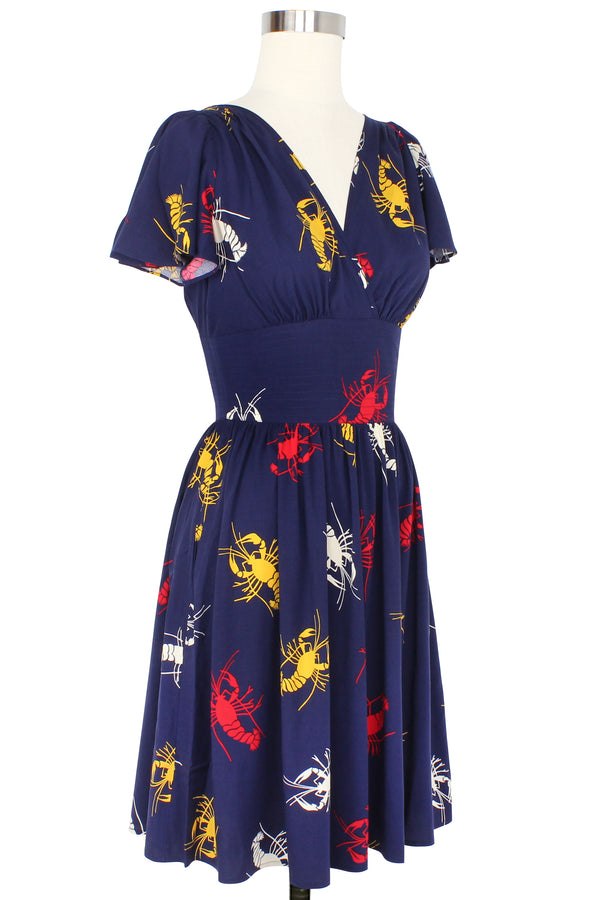 Take New Orleans home with you with our vintage-inspired Camilla Dress! This retro dress features flirty flutter sleeves before a fitted waistband, above-or-knee-length gathered skirt with pockets in our 1930s 1940s Crawfish novelty print of red, yellow, and white crustaceans on a deep navy blue background as a nod to Schiaparelli's lobster.